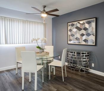 A dining room with a glass table and white chairs.